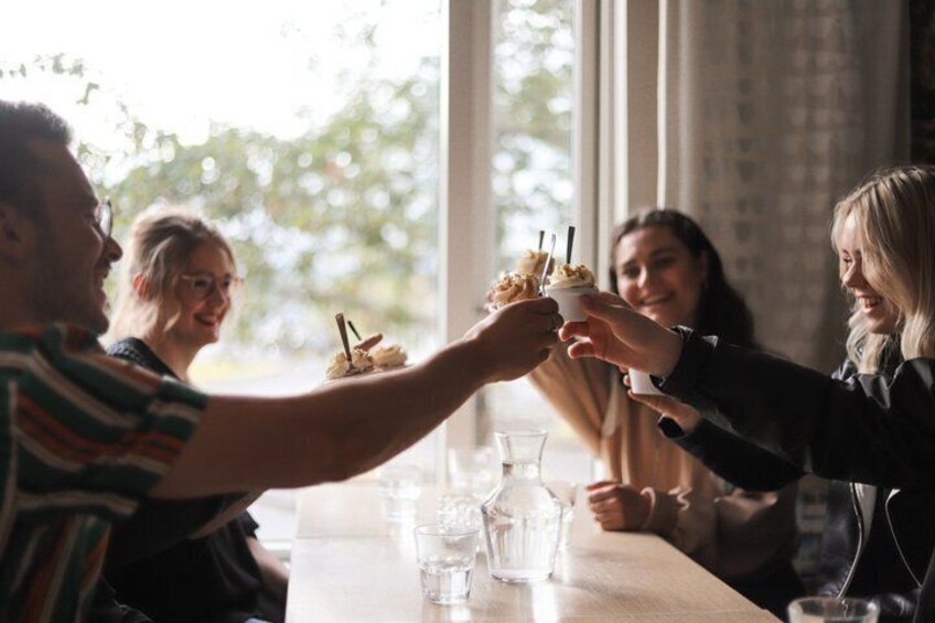 A group of people toasting with dessert cups at a table with a window in the background. 2