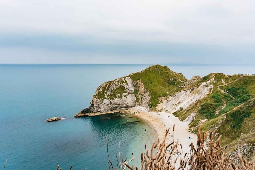 A coastal landscape with a sandy beach, rocky cliffs, and a clear blue sea. 1