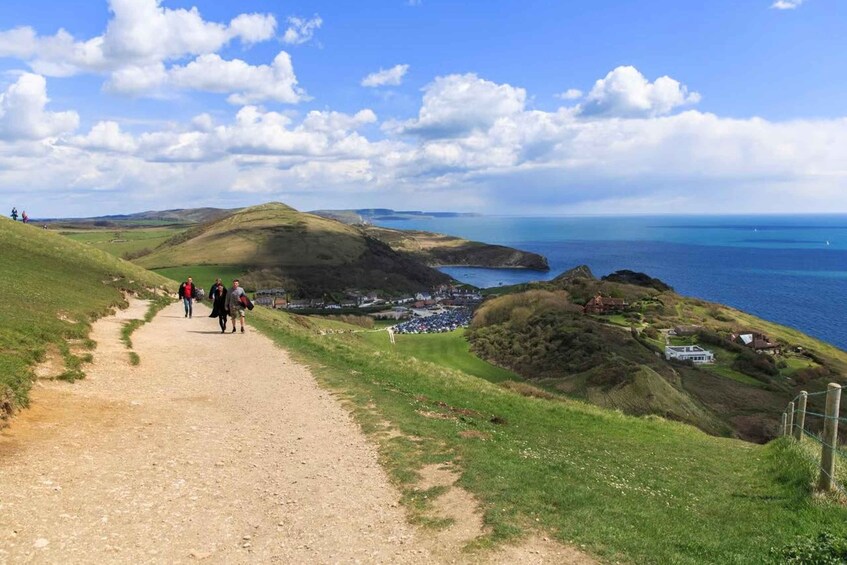 A dirt path leading to a coastal town with rolling hills and the sea in the background. 3