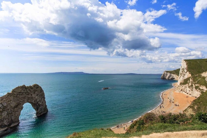 A coastal landscape with a prominent arch formation, a sandy beach, and cliffs. 4