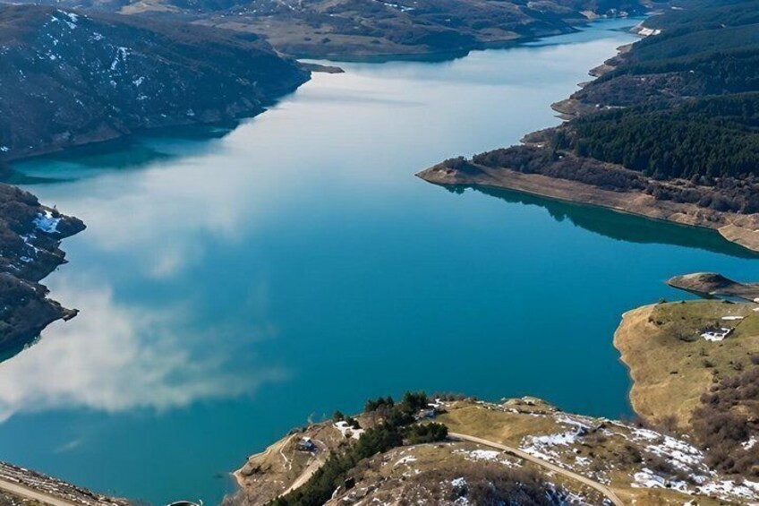 A large lake surrounded by mountains and a small island with a path leading to it. 2