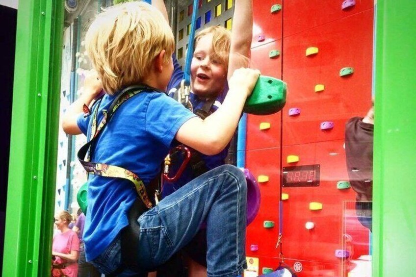 Two children climbing a red climbing wall with colorful holds. 5