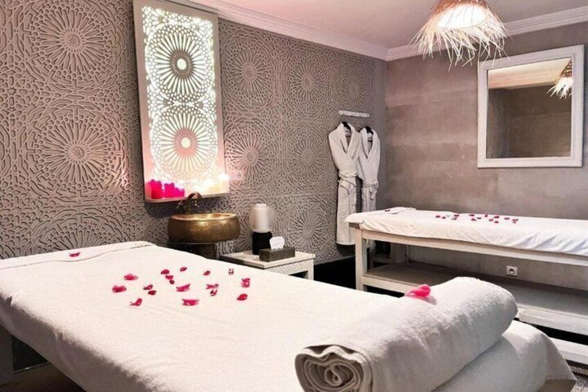 A spa room with two beds, a decorative wall, a mirror, and a sink. 1