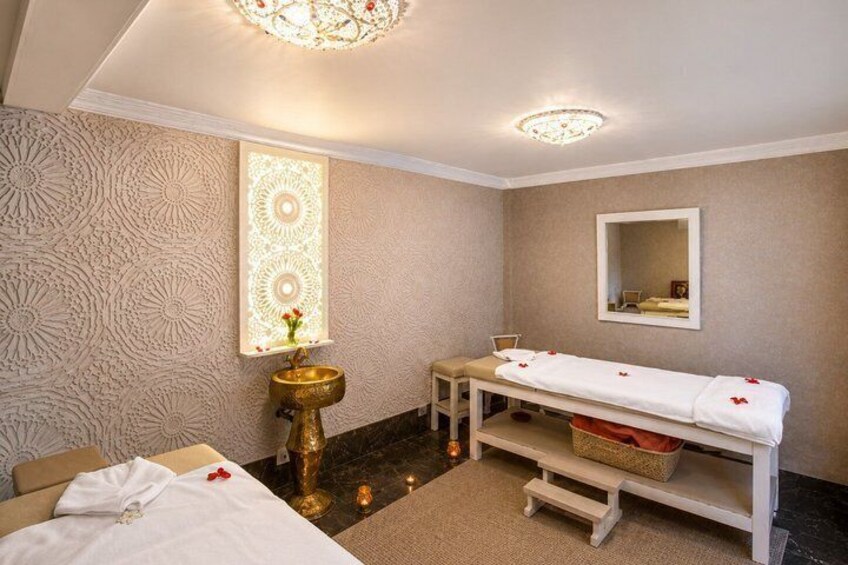 A hotel room with a bed, a bedside table, a vanity with a mirror, a wall-mounted light fixture, and a decorative wall panel. 4