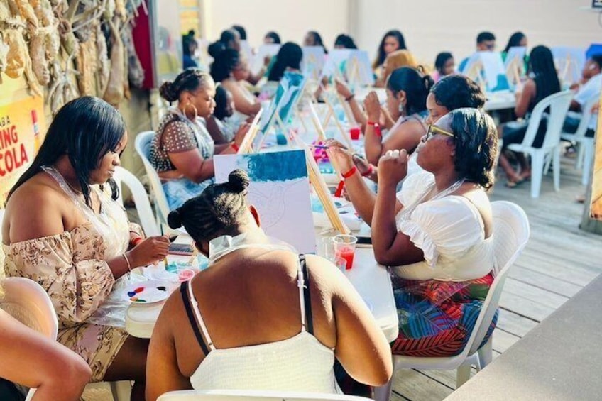 People sitting at tables outdoors, engaged in painting activities. 2