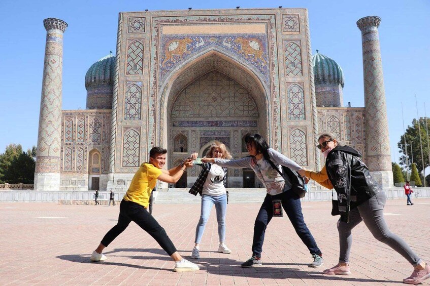 A group of people in a courtyard with a large, ornate building featuring domes and intricate tile work. 5
