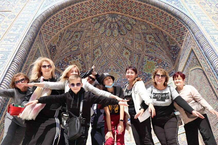 A group of people posing in front of a large, intricately patterned archway. 2