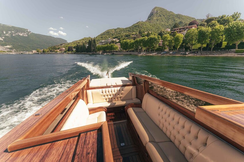 A boat with a wooden deck and cushioned seating, moving on a calm lake with a mountainous backdrop. 2