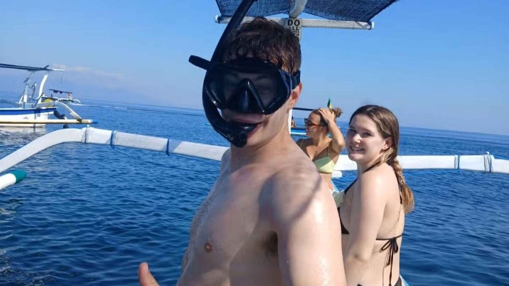 A person snorkeling with a mask and snorkel, a boat with a blue canopy, and another person in the background. 2