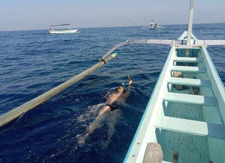 A person swimming in the ocean, a boat, and another boat in the distance. 3