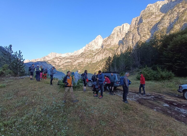 A group of hikers on a mountain trail with a car parked nearby and mountains in the background. 1
