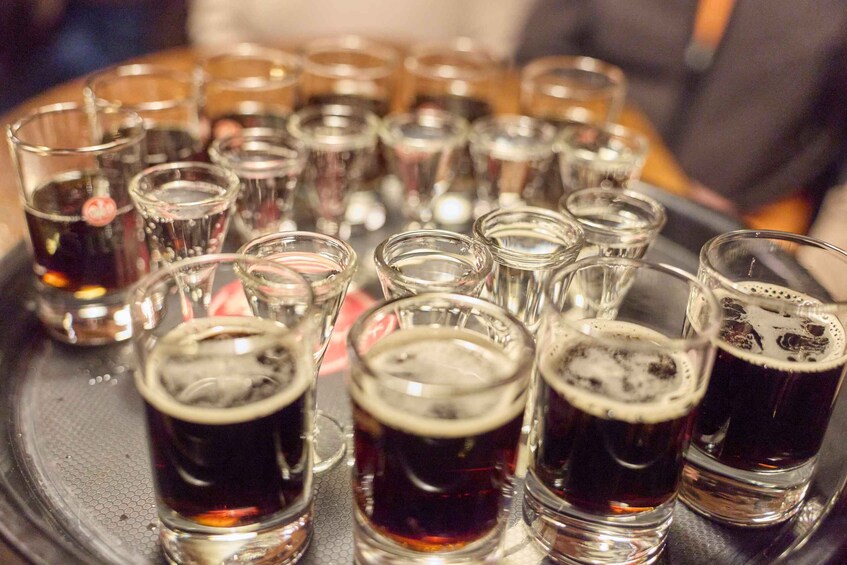 A tray of shot glasses filled with dark liquid, likely beer, with foam on top. 2