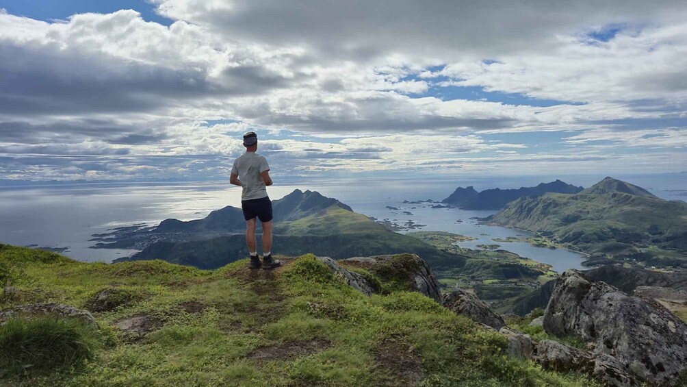 A person standing on a grassy hill overlooking a mountainous landscape with a body of water and distant islands. 2