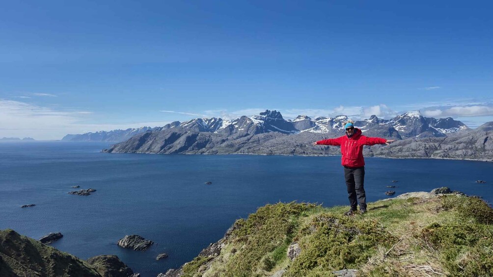 A person standing on a cliff with arms outstretched, overlooking a vast body of water and a mountain range. 3