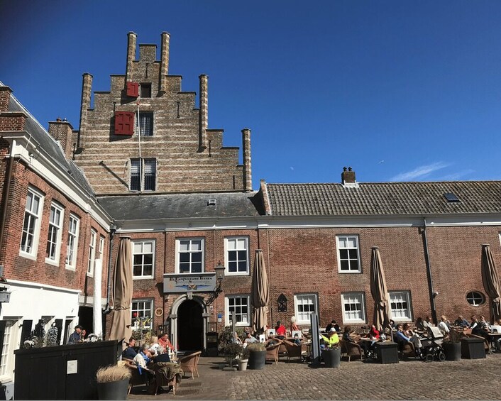 A historic building with a brick facade and a tiled roof, surrounded by outdoor seating areas with people dining. 2