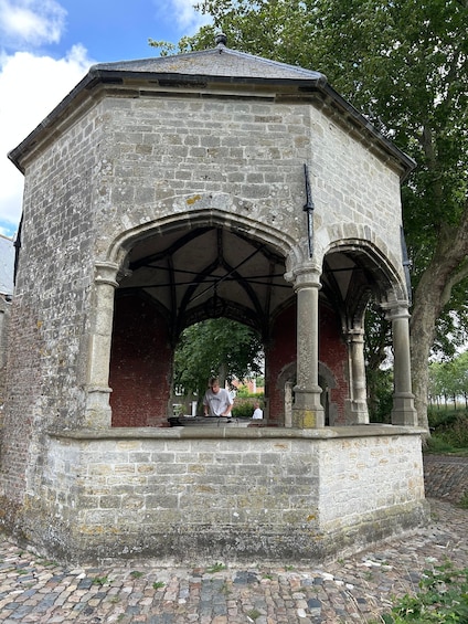 A stone gazebo with arches and columns, surrounded by trees and a cobblestone path. 4