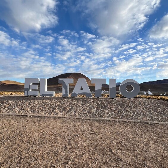 Large letters spelling 'ELATIO' on a dry, rocky terrain with a mountainous background and a partly cloudy sky. 2