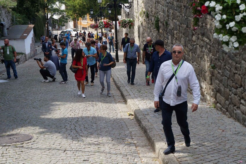 A cobblestone street with people walking, some carrying cameras, and a stone wall on one side. 5