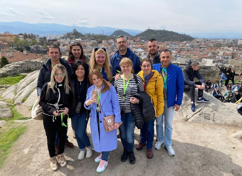 A group of people standing on a rocky outcrop overlooking a cityscape with mountains in the distance. 1