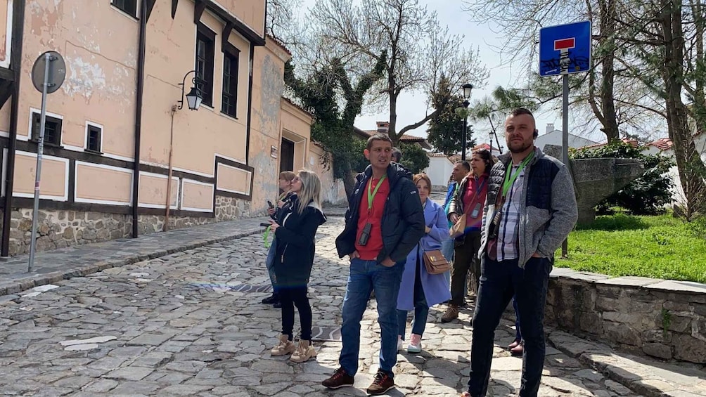 A group of people standing on a cobblestone street with a building on the left and trees in the background. 3