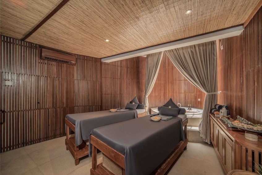 A spa room with wooden paneling, two massage tables, a small sink, and a vanity with toiletries. 4