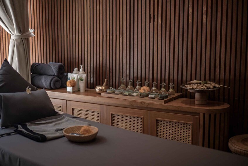 A spa-like setting with a massage table, pillows, a wooden panel wall, and various spa products on a counter. 3