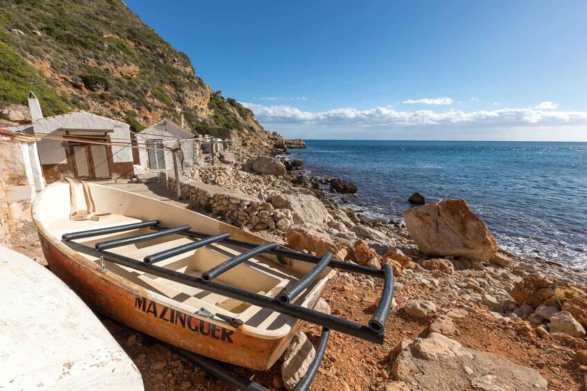 A rocky beach with a small boat named 'MAZINGUEK' and a building in the background. 3
