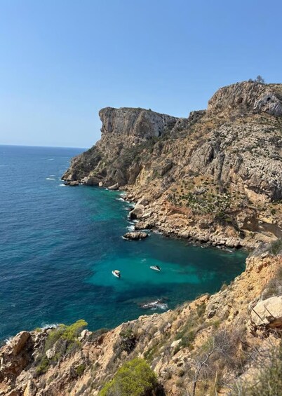 A rocky coastline with clear blue waters and a few small boats anchored near the shore. 5