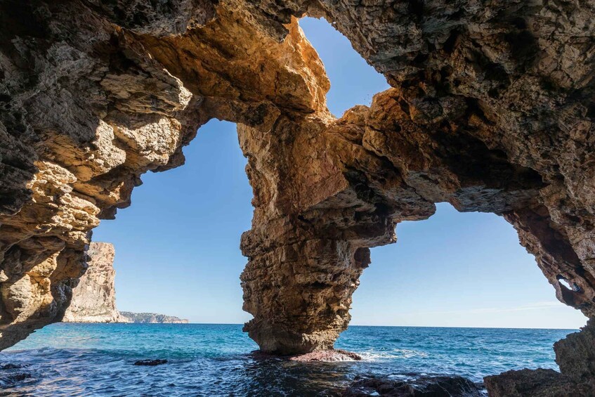 A natural rock formation with a cave-like opening and a view of the sea. 1
