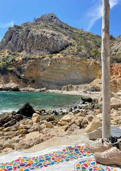A rocky beach with clear turquoise water, a large cliff, and a wooden pole. 4