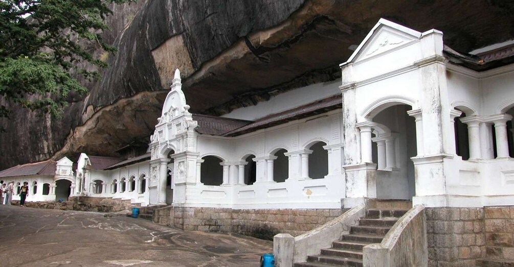 Ein weißer Tempel mit mehreren Bögen und einer Treppe, die zu ihm hinaufführt, vor einer felsigen Klippenlandschaft. 5