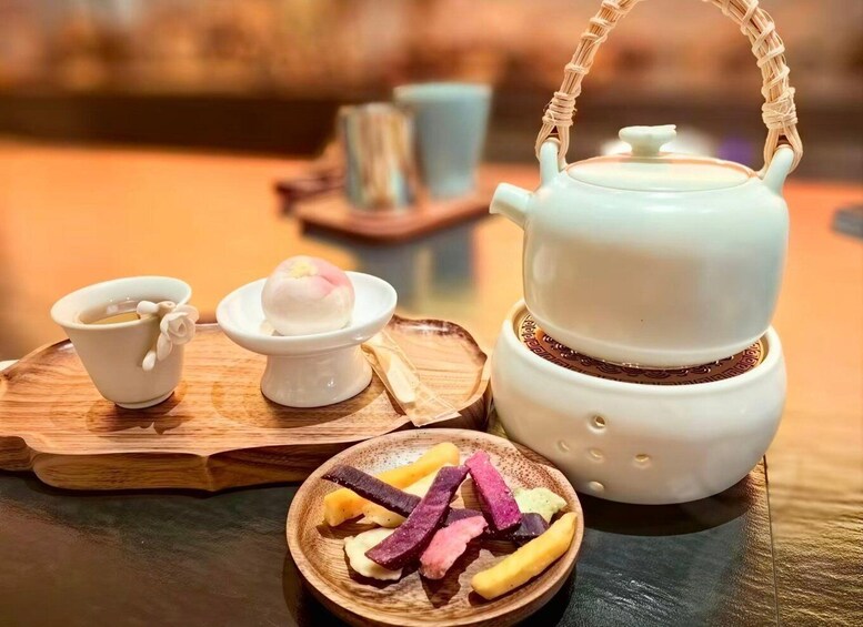 A traditional tea set with a teapot, cups, and a wooden tray with snacks. 3