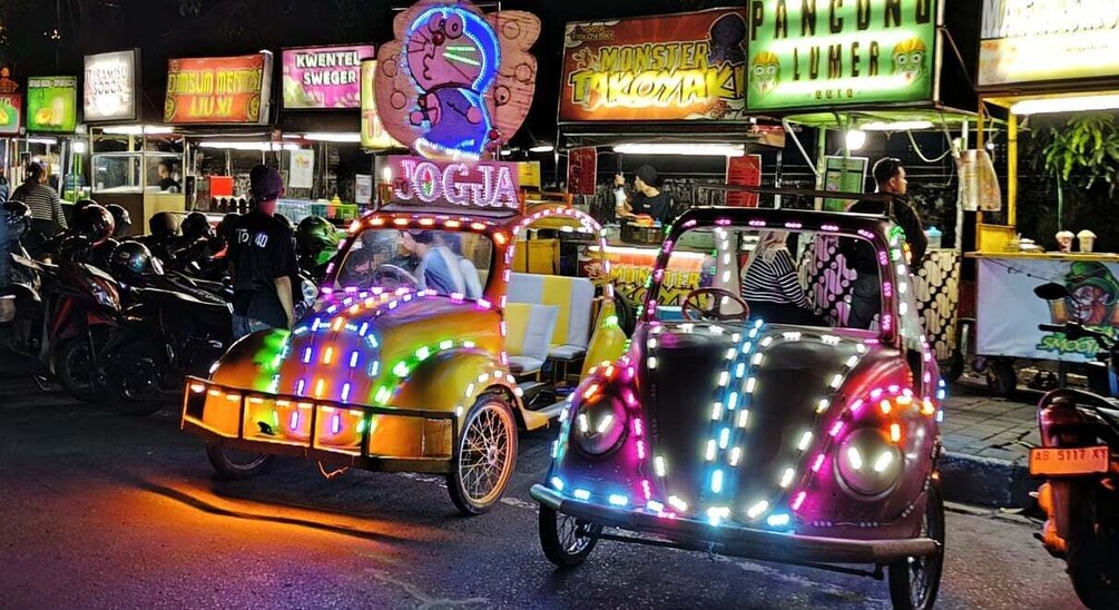 Two brightly lit, decorated vehicles with neon lights and signs, parked on a street at night. 3
