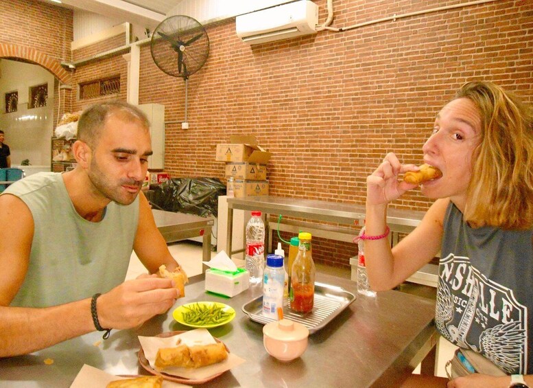 Two people eating at a table with food and condiments. 5