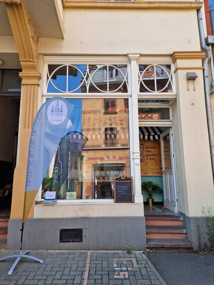 A storefront with a large window, a sign reading 'MAINZ CITYTOURS,' and a chalkboard with a welcome message. 5