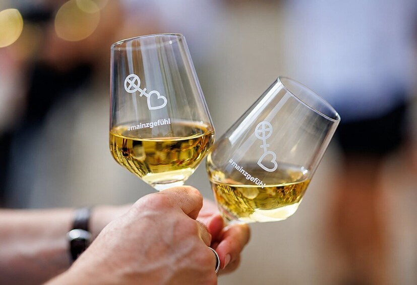 Two hands holding wine glasses with etched designs and the hashtag #mainzgefuhl. 1