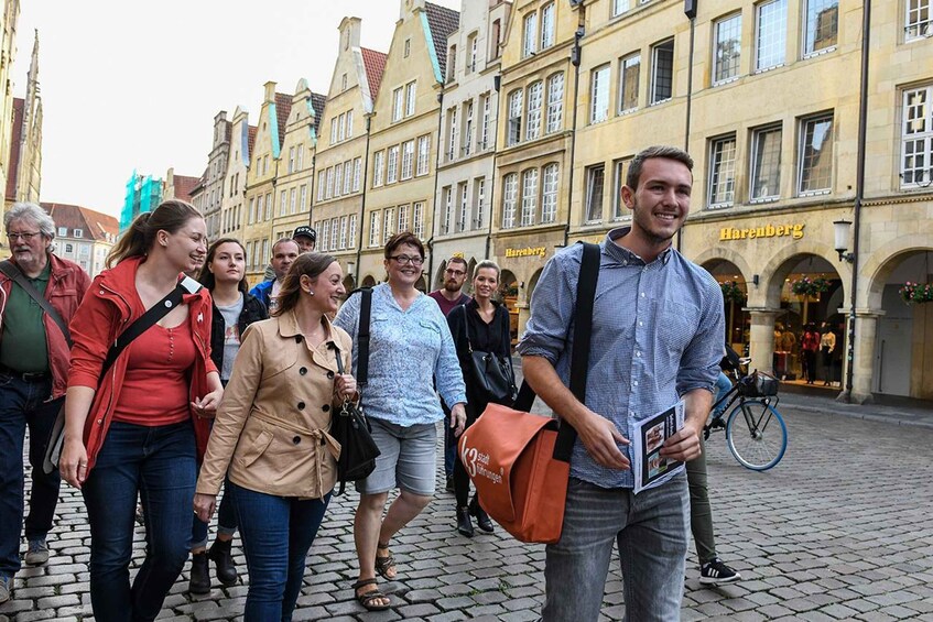 A group of people walking on a cobblestone street in front of historic buildings with a shop named 'Harenberg' visible. 5