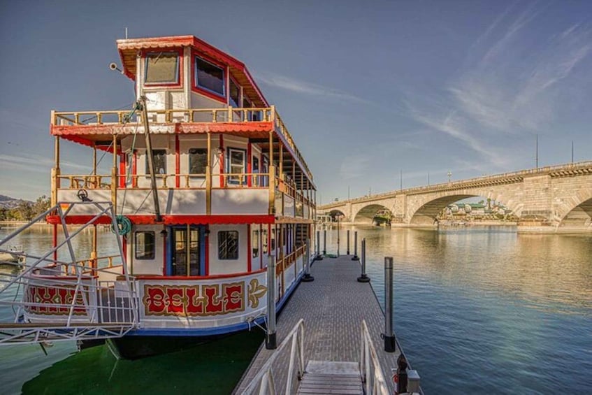 A double-decked boat docked at a pier with a stone bridge in the background. 2