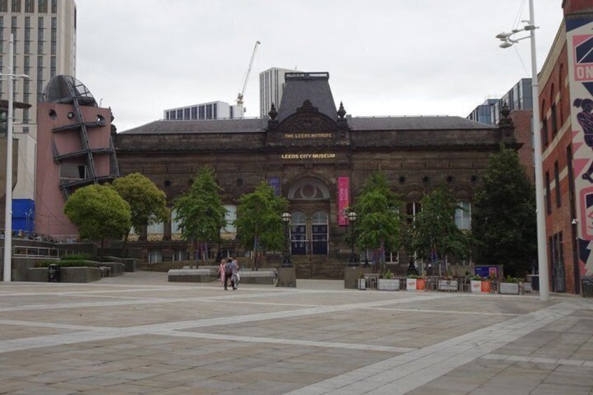 A large building with a prominent entrance, surrounded by trees and a paved plaza. 4