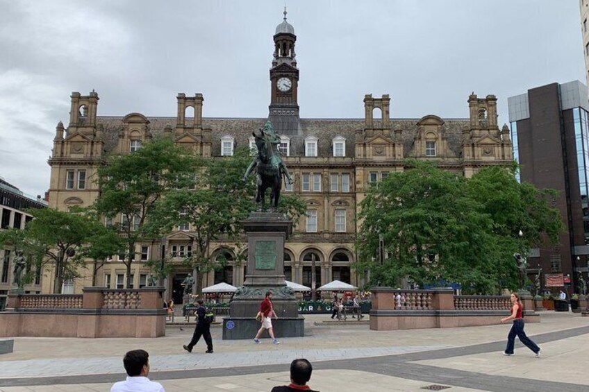 A historic building with a clock tower, a statue, and a fountain in a public square. 1