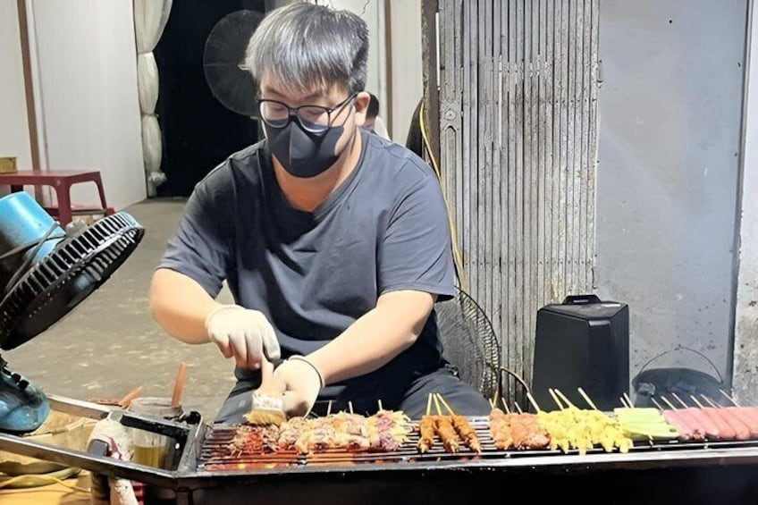 A person grilling skewers on a portable stove. 1