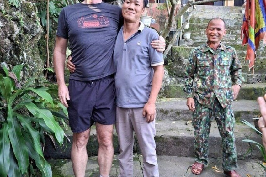 Three people standing outdoors with greenery and stairs in the background. 5