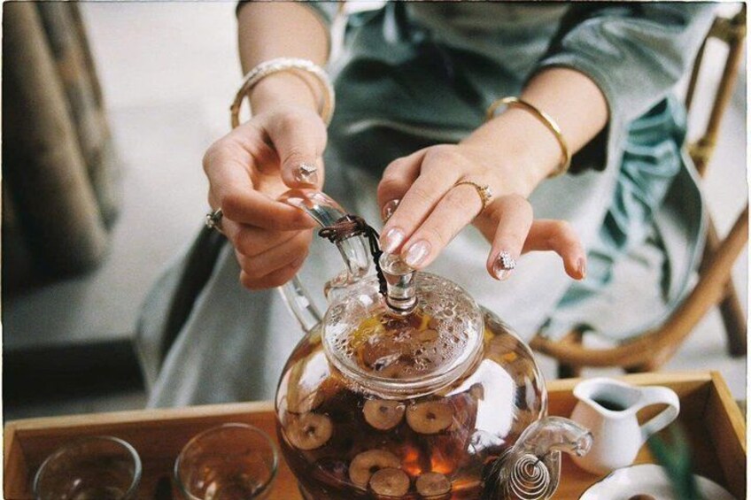 A person pouring tea from a glass teapot into a cup. 3