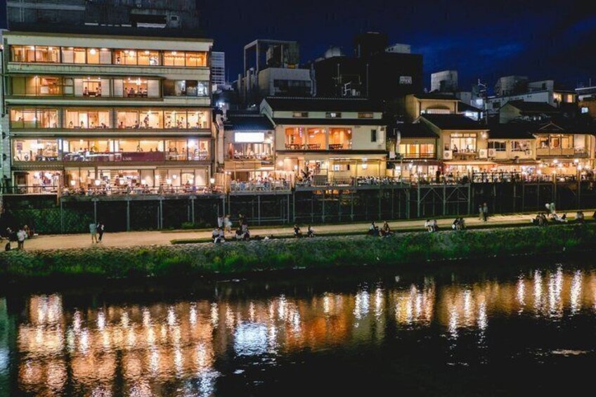 A riverside view of a lit-up building complex with reflections on the water. 5