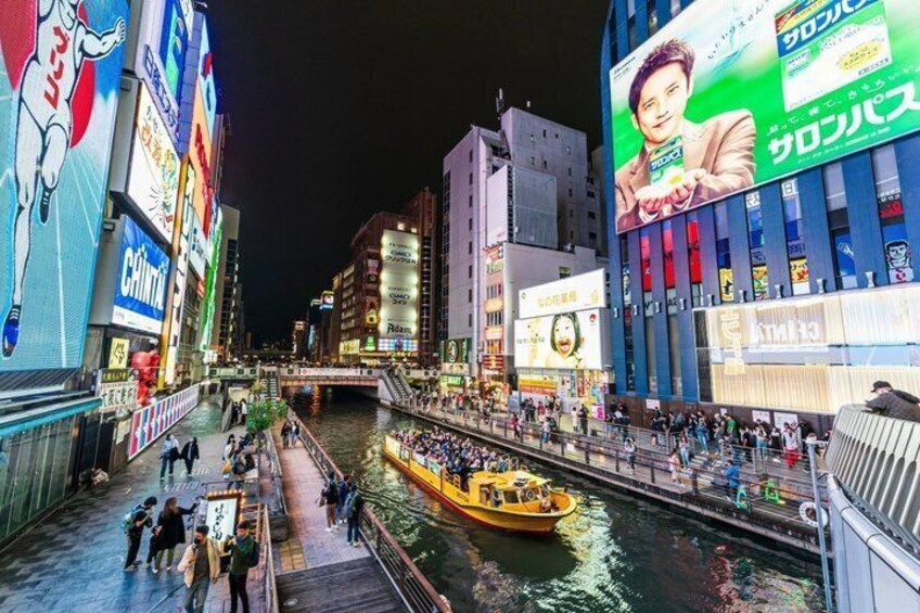 A river with a boat, buildings with advertisements, and a pedestrian walkway. 3