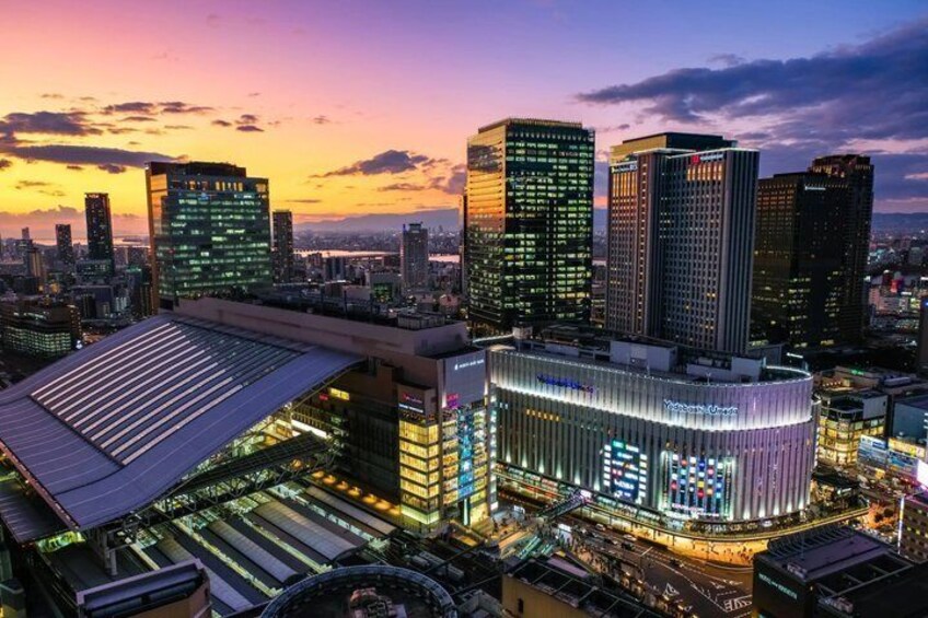 A cityscape at dusk with illuminated buildings and a prominent modern structure with a curved facade. 2