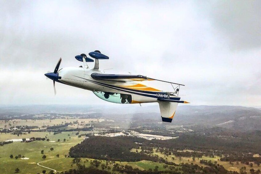 A small aircraft flying over a landscape with fields and hills. 1
