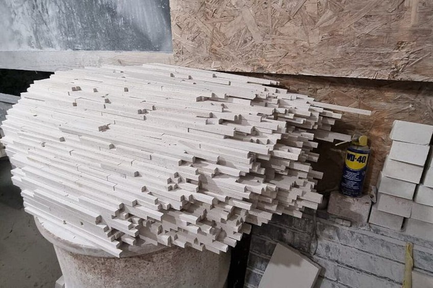 A large stack of white rectangular blocks with holes, possibly for construction or manufacturing, in a workshop setting. 4