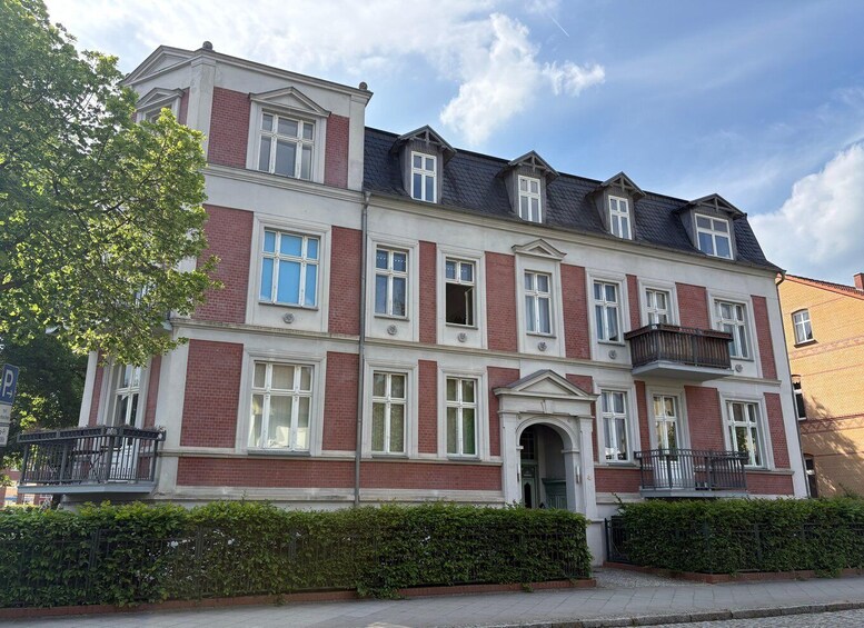 A multi-story residential building with red brick and white trim, large windows, and a dark roof. 3