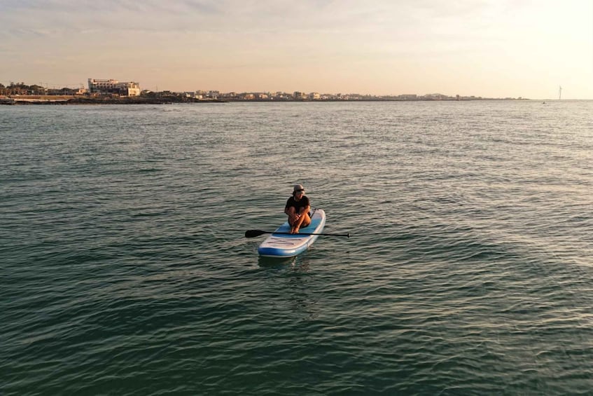 A person paddleboarding on a calm sea with buildings in the background. 4